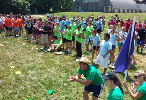 Teams enthusiastically competing in a relay race during the Outrageous Games team building event, surrounded by a crowd of cheering participants.