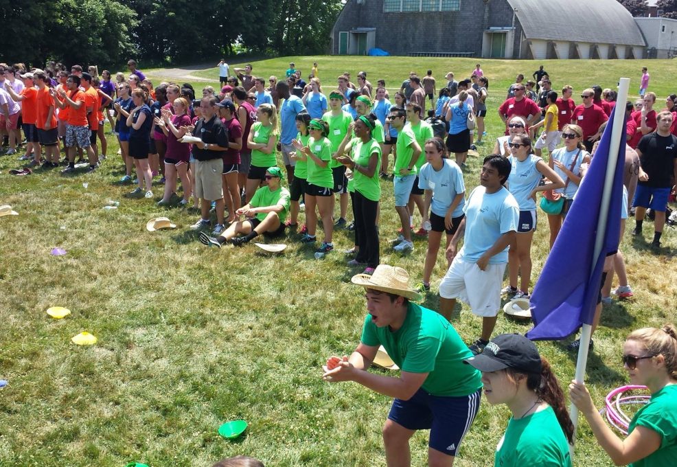 Teams enthusiastically competing in a relay race during the Outrageous Games team building event, surrounded by a crowd of cheering participants.