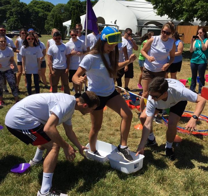 Participants in white shirts engage in a fun and wacky relay challenge during an Outrageous Games team building event, with one person wearing a snorkel mask.