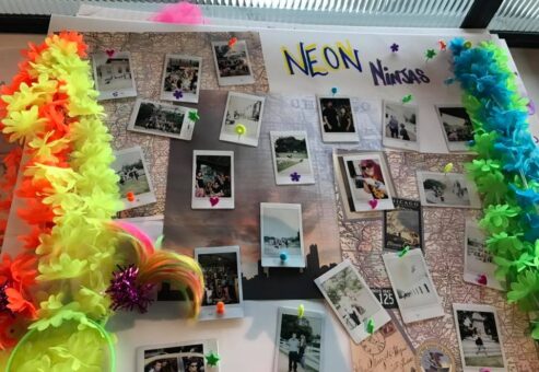 A vibrant display board titled 'Neon Ninjas' from a Polaroid scavenger hunt, decorated with colorful leis and neon accents. The board features a collection of Polaroid photos pinned around a central map, capturing fun moments from the scavenger hunt challenges. The lively decorations and creative photo arrangement highlight the energy and excitement of the team building event.