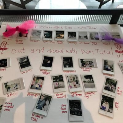 A display board from a Polaroid scavenger hunt themed 'Out and About with Team Tutu.' The board features instant photos taken at Lincoln Park Zoo, adorned with hand-drawn stick figures in tutus and decorated with small pink and purple tutu accents. Each photo is captioned with playful notes about team challenges and activities, showcasing the fun and lighthearted atmosphere of this creative team building event. thumbnail