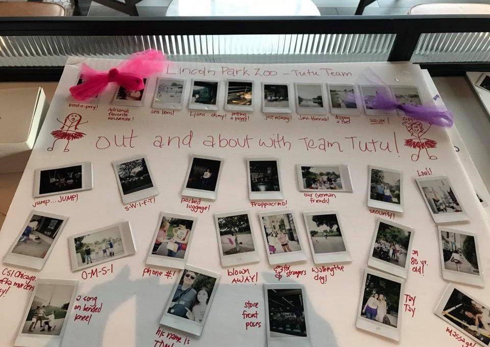 A display board from a Polaroid scavenger hunt themed 'Out and About with Team Tutu.' The board features instant photos taken at Lincoln Park Zoo, adorned with hand-drawn stick figures in tutus and decorated with small pink and purple tutu accents. Each photo is captioned with playful notes about team challenges and activities, showcasing the fun and lighthearted atmosphere of this creative team building event.