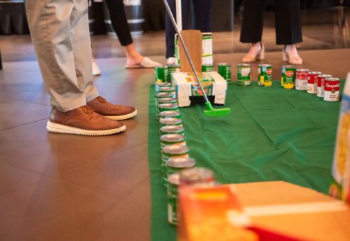 Participants play on a custom-built mini golf course made from canned goods and other non-perishable food items during a 'Build Your Own Mini Golf Course' team building event.