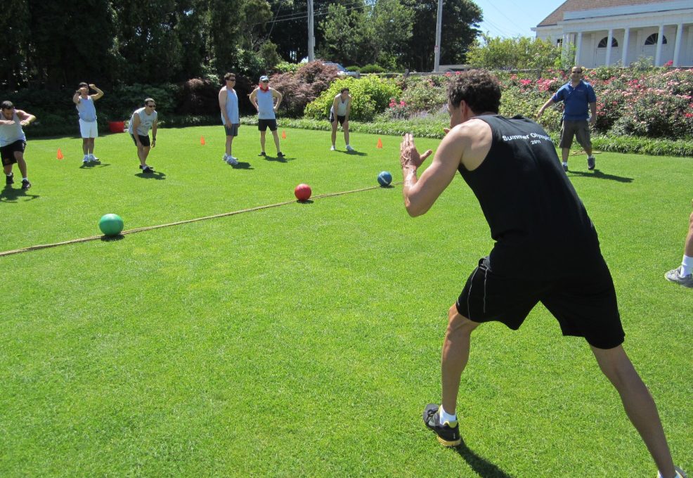 Participants gearing up for a dodgeball challenge during the Outrageous Games team building event on a sunny lawn.
