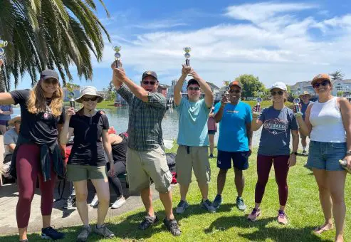 Team members celebrating with trophies after successfully completing the Build-A-Boat team building challenge by the water.