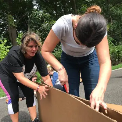 Team members cutting cardboard to construct their boat during the Build-A-Boat team building activity. thumbnail