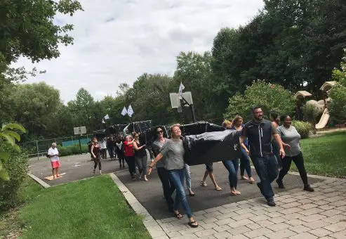 Participants carrying their completed cardboard boats to the water during the Build-A-Boat team building challenge.