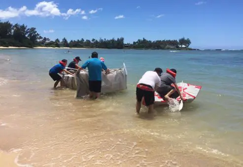 Teams launching their handmade cardboard boats into the water during the Build-A-Boat team building challenge on a sunny beach.