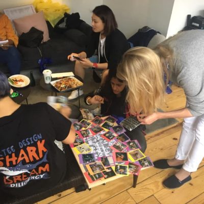 A dynamic scene of team members assembling a collage on the floor, using Polaroid photos from a team building scavenger hunt. Individuals focus on arranging the photos, and enjoying light snacks. The activity fosters teamwork and creativity. thumbnail