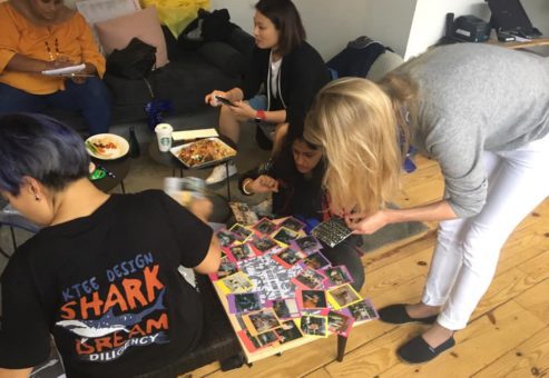A dynamic scene of team members assembling a collage on the floor, using Polaroid photos from a team building scavenger hunt. Individuals focus on arranging the photos, and enjoying light snacks. The activity fosters teamwork and creativity.