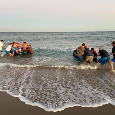 Participants launching their cardboard boats into the ocean during the Build-A-Boat team building challenge. thumbnail