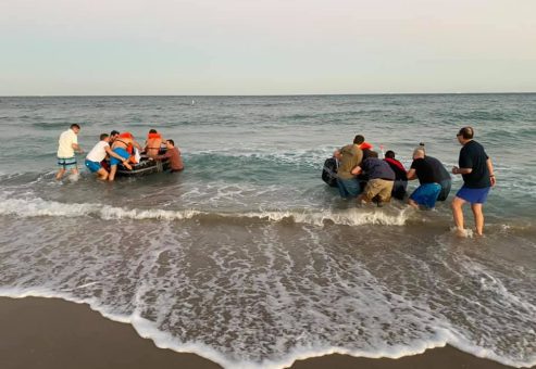Participants launching their cardboard boats into the ocean during the Build-A-Boat team building challenge.