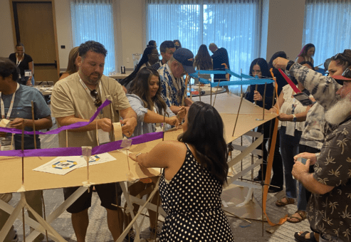 articipants in the Bridging the Divide team building activity work together to construct a large, collaborative bridge.