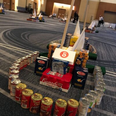 A mini golf course hole constructed from food cans, cereal boxes, and other non-perishable items during a 'Build Your Own Mini Golf Course' team building event. thumbnail