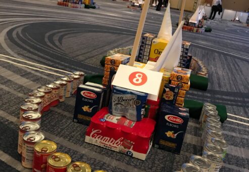 A mini golf course hole constructed from food cans, cereal boxes, and other non-perishable items during a 'Build Your Own Mini Golf Course' team building event.