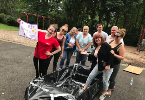 Team posing proudly next to their completed cardboard boat during the Build-A-Boat team building challenge.