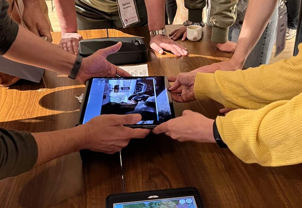 Participants in a 'Corporate CSI' team building event gather around a table, using iPads to examine digital evidence and clues as they work collaboratively to solve the mystery.