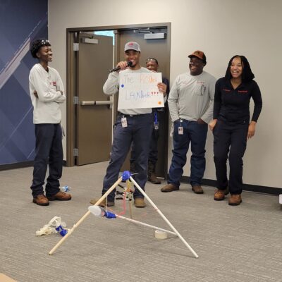 A team presenting their catapult design called 'The Rocket Launcher' during an indoor segment of the Catapult to Success team building activity, showcasing creativity, teamwork, and presentation skills. thumbnail