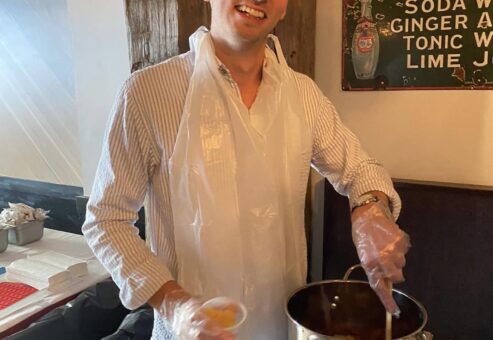 Smiling participant stirring a pot during the Wicked Good Chowda Cook-Off team building event.