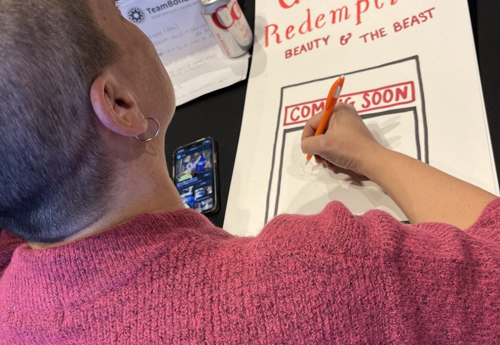 A participant draws a poster titled 'Gaston's Redemption: Beauty & The Beast' during a team building activity, showcasing creativity.