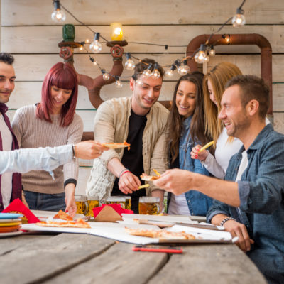 Team members sharing slices of pizza in a relaxed, outdoor setting during The Ultimate Pizza Challenge team building event.