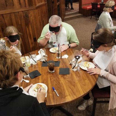 A group of participants at a Dining in the Dark team building event, engaging in a sensory dining experience while blindfolded. thumbnail