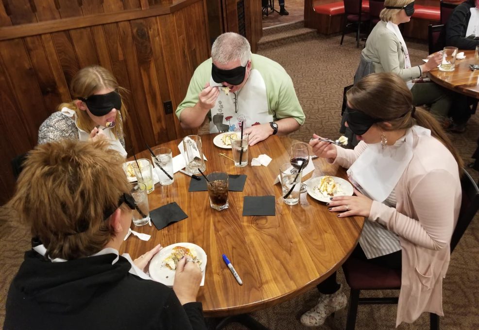 A group of participants at a Dining in the Dark team building event, engaging in a sensory dining experience while blindfolded.