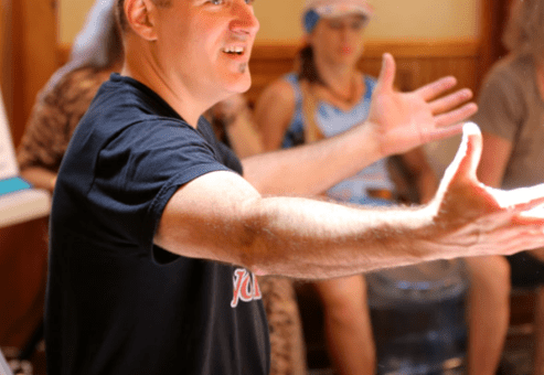 A facilitator leads the Drumming Up A Team event, encouraging participants to connect through rhythm and teamwork, with a vibrant and engaging group dynamic.