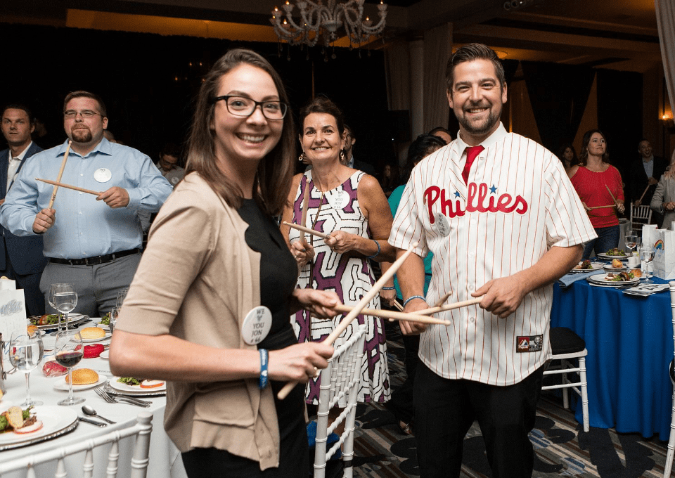 Participants in the Drumming Up A Team event enthusiastically engage in a percussion activity, fostering unity and teamwork while creating an upbeat atmosphere of collaboration and celebration.