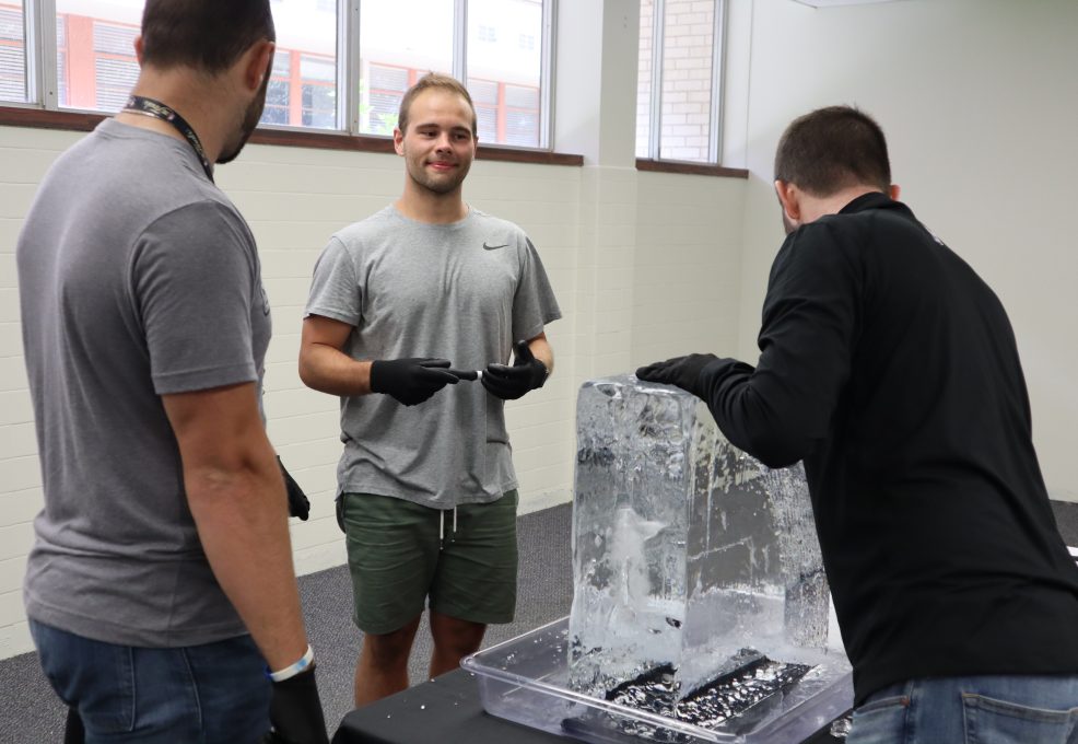 A group of participants works together, chiseling an ice block during a Team building Ice Sculpting event, showcasing teamwork and creativity.
