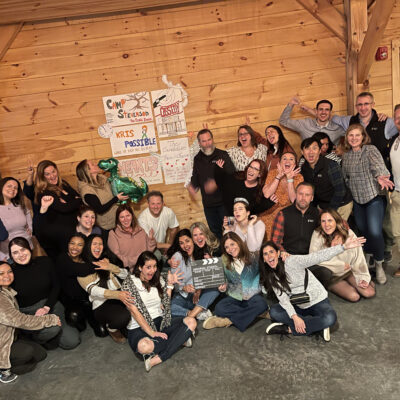 A large group of participants poses enthusiastically in front of handmade posters during a film festival movie making team building event. thumbnail