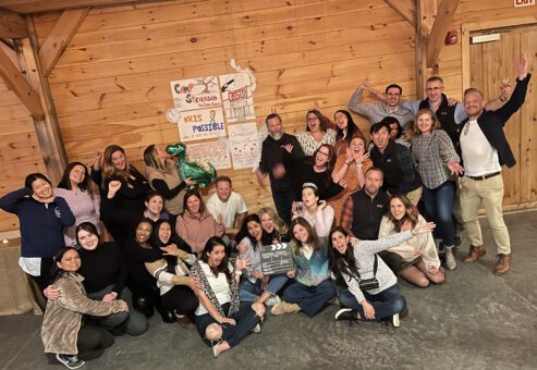 A large group of participants poses enthusiastically in front of handmade posters during a film festival movie making team building event.