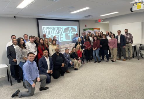 Group photo of participants after completing their Operation Military Care team building event, with care packages ready to be sent to U.S. troops.