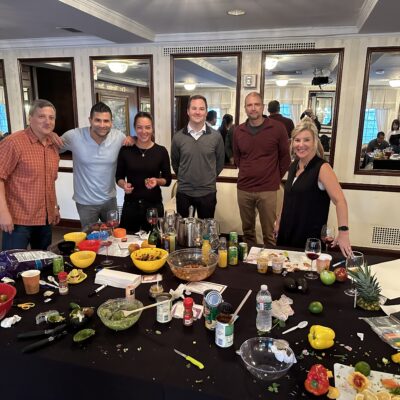 A team celebrating after completing the Salsa Showdown, surrounded by a variety of colorful ingredients, freshly made salsa, and drinks, showcasing the fun and competitive spirit of the event. thumbnail