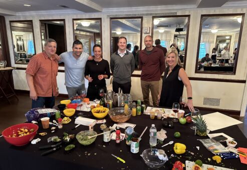A team celebrating after completing the Salsa Showdown, surrounded by a variety of colorful ingredients, freshly made salsa, and drinks, showcasing the fun and competitive spirit of the event.