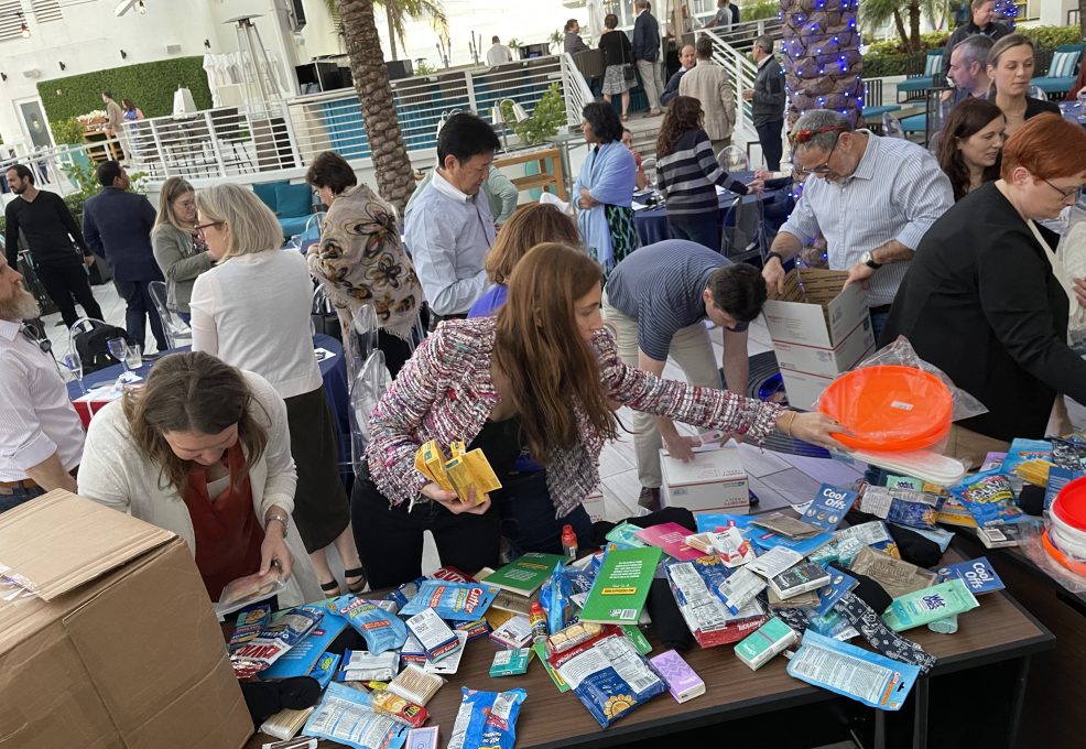 Participants enthusiastically packing care packages for troops during an outdoor Operation Military Care team building event.
