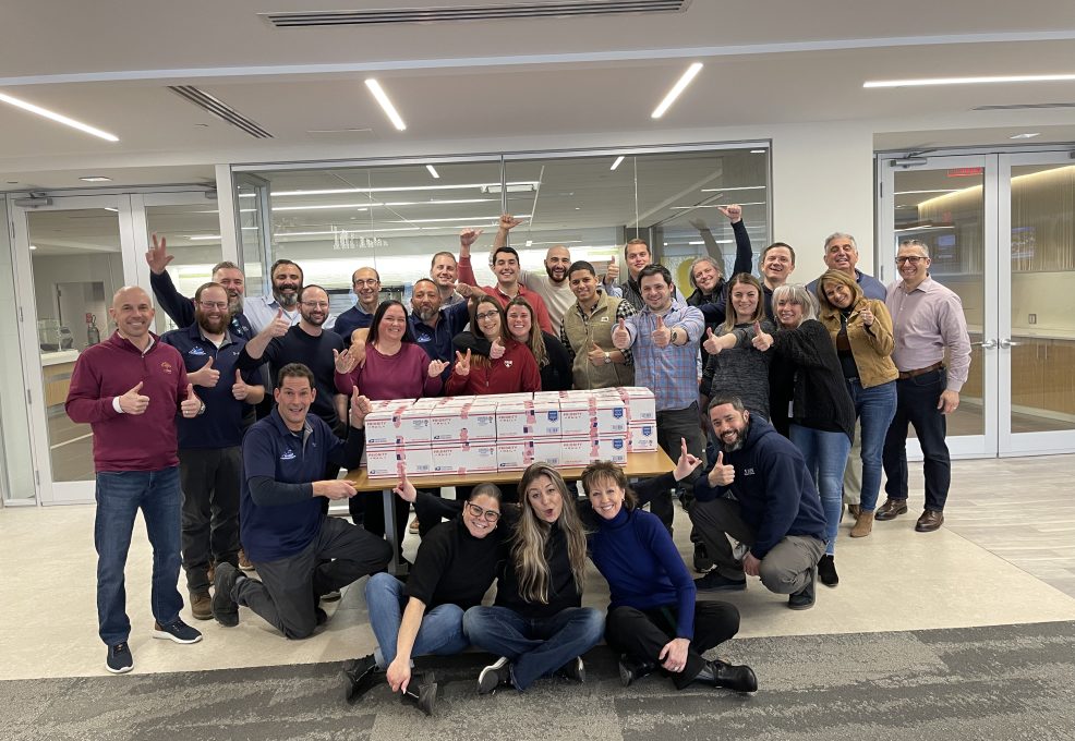 Team poses with completed care packages during the Operation Military Care team building event, ready to be sent to military personnel overseas.