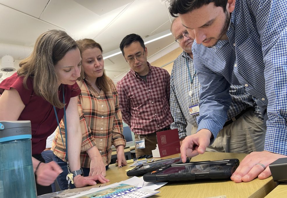 Team members collaboratively examining a virtual crime scene on a tablet during the Corporate CSI team building activity.
