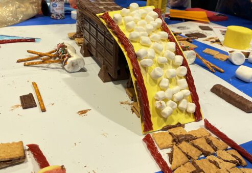 A chocolate bridge, covered with marshmallows and licorice, is creatively constructed during The Chocolate Challenge team building event, highlighting teamwork and edible engineering.