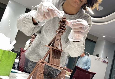 A participant in the Chocolate Challenge team building event carefully stacks chocolate bars to create a stable structure, focusing on precision and creativity.