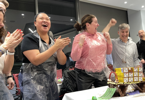 Team members celebrate their success in the Chocolate Challenge team building event, excitedly clapping after constructing their chocolate bridge.