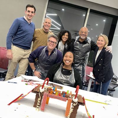 A team proudly poses with their creative, candy-decorated chocolate bridge after completing the Chocolate Challenge team building event, showcasing teamwork and fun. thumbnail