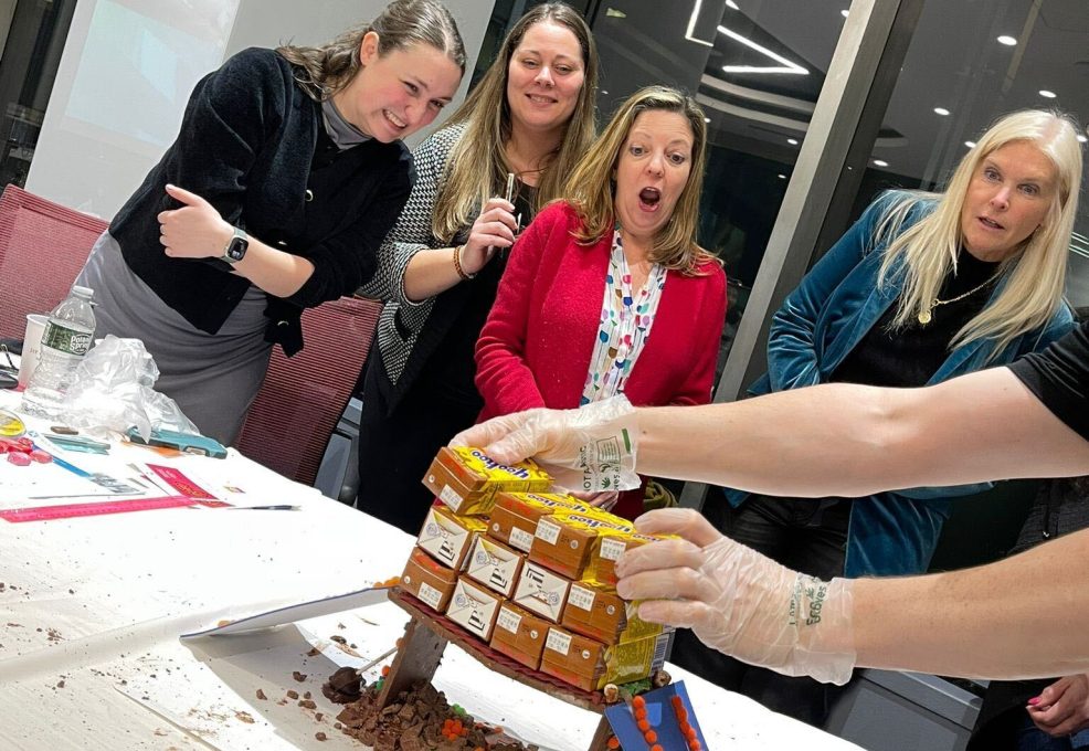 Participants in the Chocolate Challenge team building event express excitement as they successfully unveil their chocolate bridge structure, decorated with candies and icing.