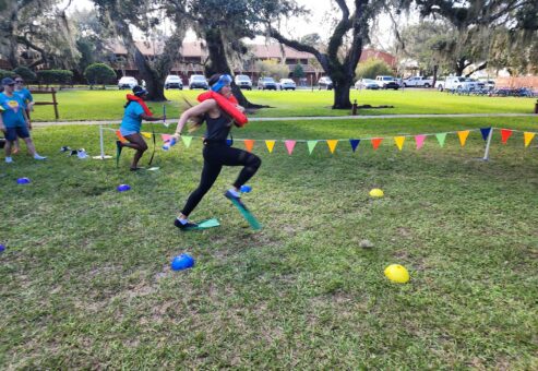 A participant wearing a life vest and flippers runs through an obstacle course during the Outrageous Games team building event, showcasing fun and friendly competition.
