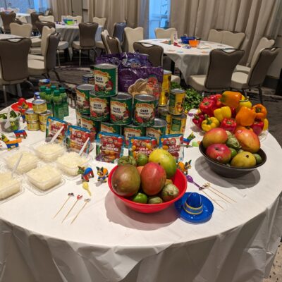A vibrant setup of fresh fruits, including mangoes and peppers, along with canned ingredients for the Salsa Showdown team building event, featuring colorful decorations. thumbnail