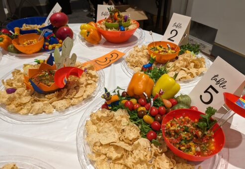 Colorful bowls of salsa and fresh ingredients, surrounded by tortilla chips and labeled for different teams during the Salsa Showdown team building event.