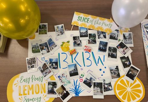 A creative Polaroid photo display from a scavenger hunt event, arranged on a table with colorful signs and balloons. The board features an assortment of instant photos capturing team activities and moments of fun, surrounded by playful lemon-themed decorations like 'Easy Peasy Lemon Squeezy' and 'Slice of the Party.' The display highlights the artistic and celebratory atmosphere of the team building activity.