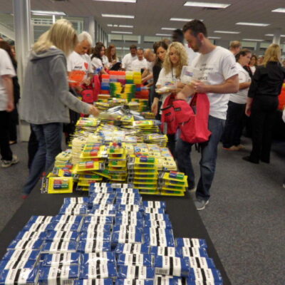 Team building participants are organizing and packing school supplies, including notebooks, pencils, and backpacks, at a Tools for Schools CSR program. thumbnail
