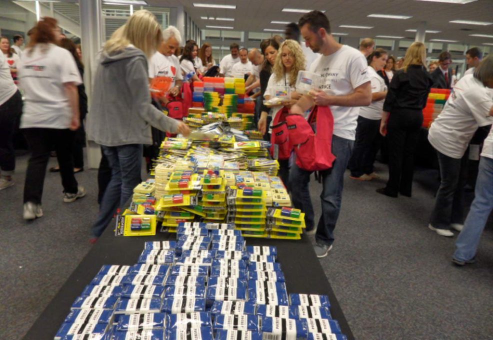 Team building participants are organizing and packing school supplies, including notebooks, pencils, and backpacks, at a Tools for Schools CSR program.