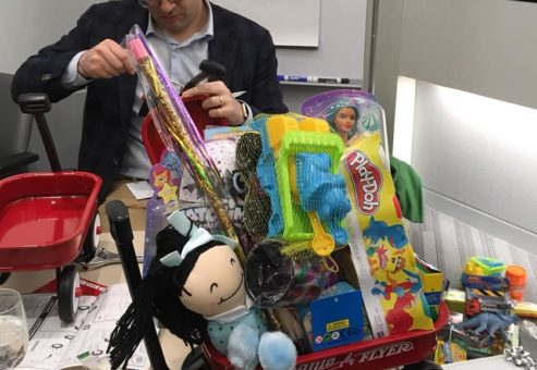 Participant assembling a wagon filled with toys during a charitable holiday team building activity.